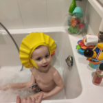 a toddler in a foam bath with a bath hat washing his hair