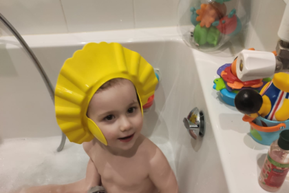 a toddler in a foam bath with a bath hat washing his hair