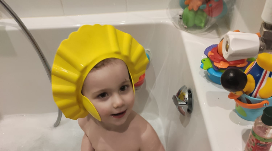 a toddler in a foam bath with a bath hat washing his hair