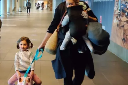 Maman dans un aéroport avec un bébé en porte-bébé et une petite fille sur une valise à roulettes pour enfant